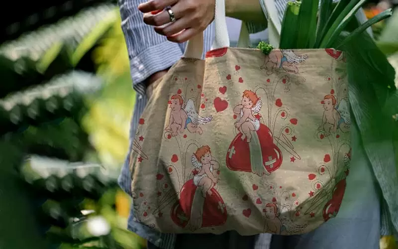 A preview of an angel cupid sitting on a red heart design pattern used on a hand bag